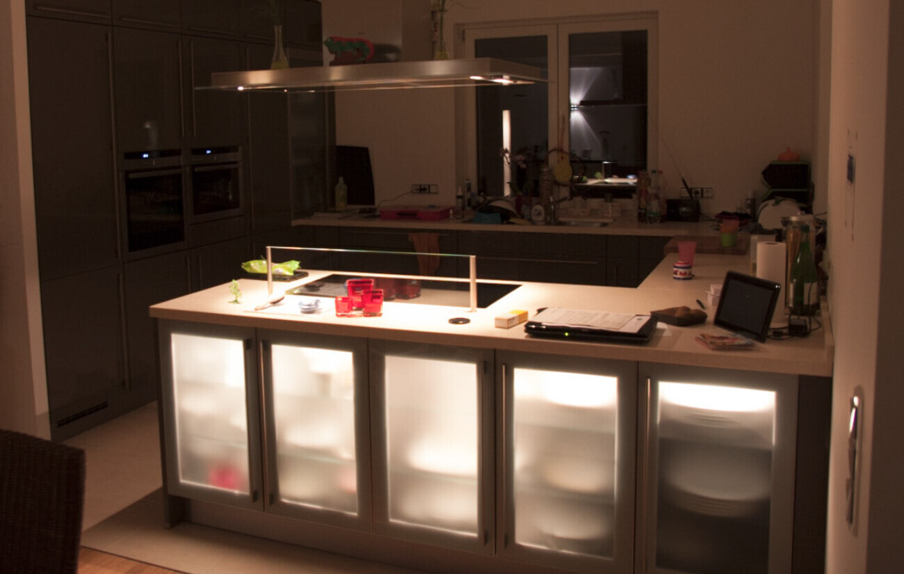 Moderne Küche mit Insel, beleuchteten Glasvitrinen und Wandbacköfen.