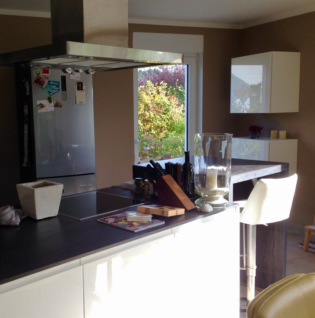 Moderne Küche mit Insel, Kühlschrank links, Glaskerzenhalter und Fensterblick ins Grüne.