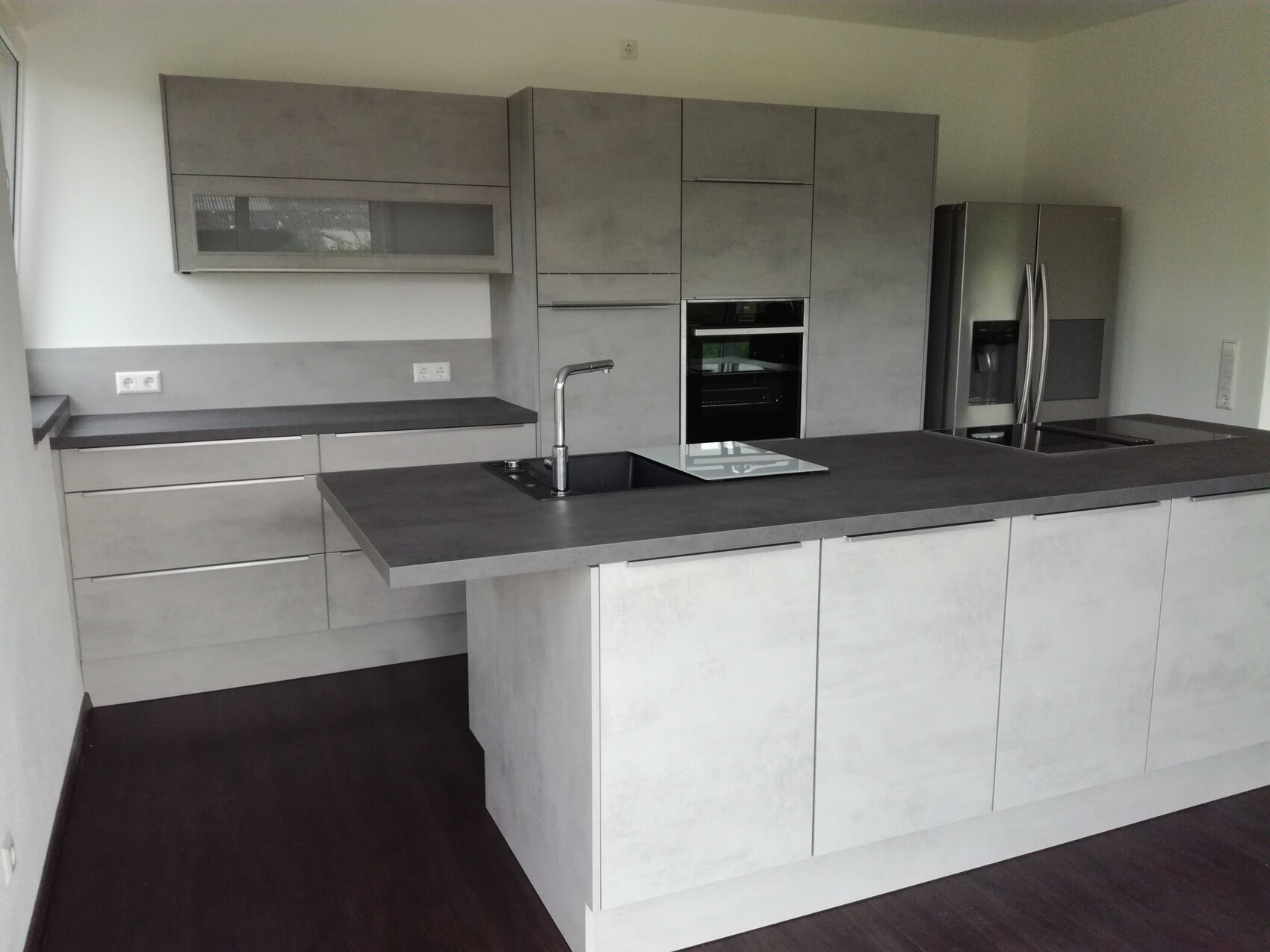 Moderne graue Küche mit Insel, Spüle, Induktionskochfeld, Backofen und Kühlschrank.