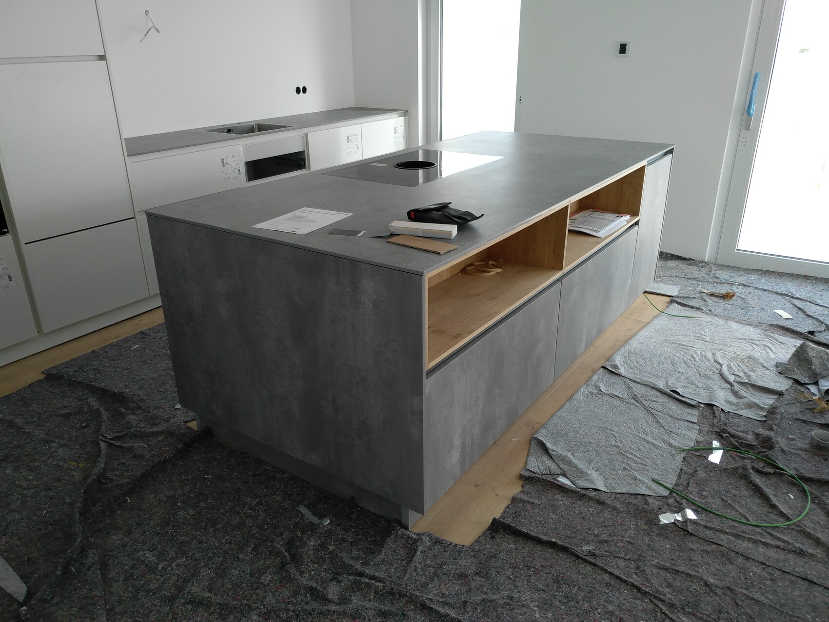 Küche im Bau: Beton-Insel mit offenen Fächern, weiße Fronten, Bodenabdeckung