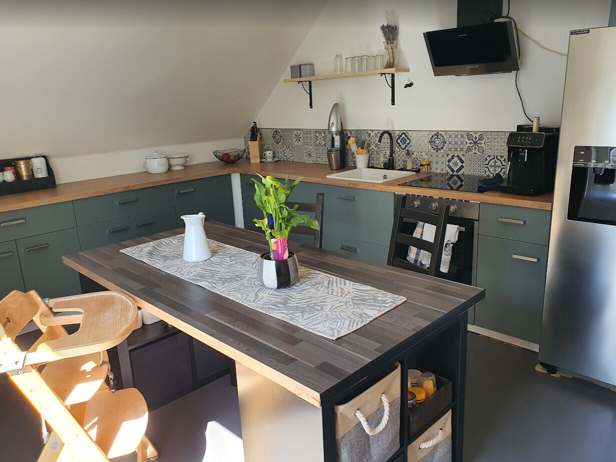 Moderne Küche mit Insel, grünen Unterschränken, Holzplatte, Spüle, Kaffeemaschine und Pflanze.