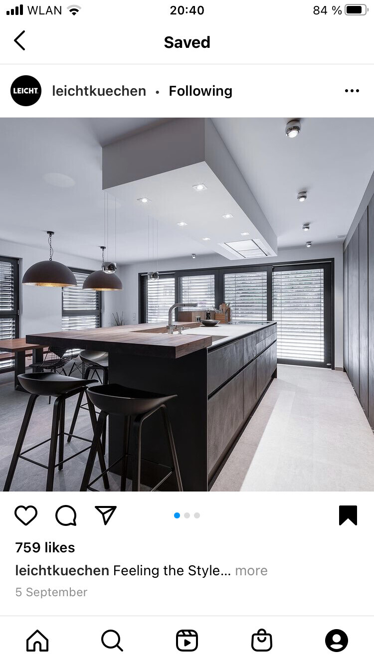Moderne Küche mit Insel, dunklen Unterschränken, Holzarbeitsplatte, Hängelampen und großen Fenstern.