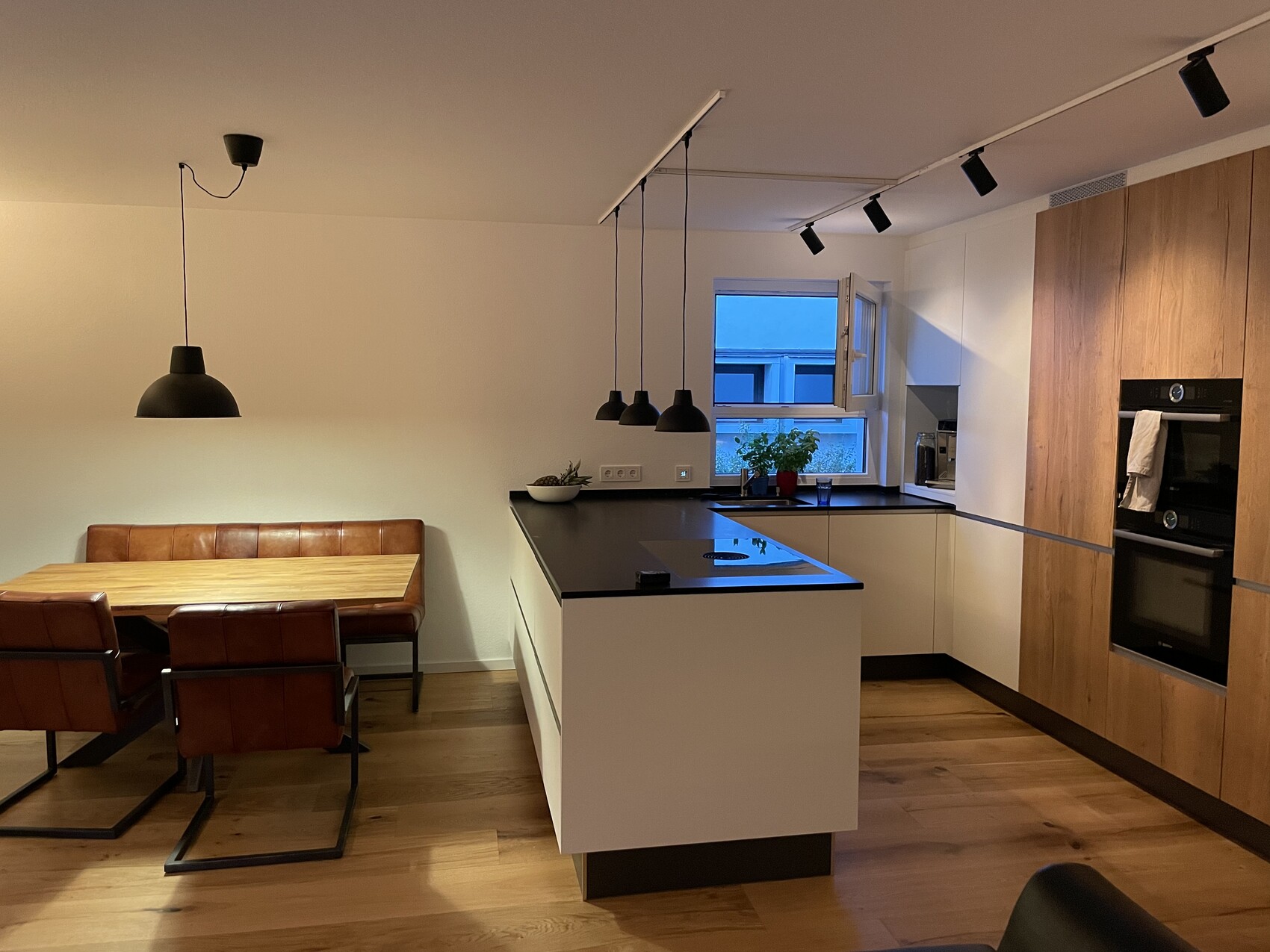 Moderne Küche mit Insel, schwarzen Arbeitsplatten, Holzschränken und Esstisch mit braunen Ledersitzen.