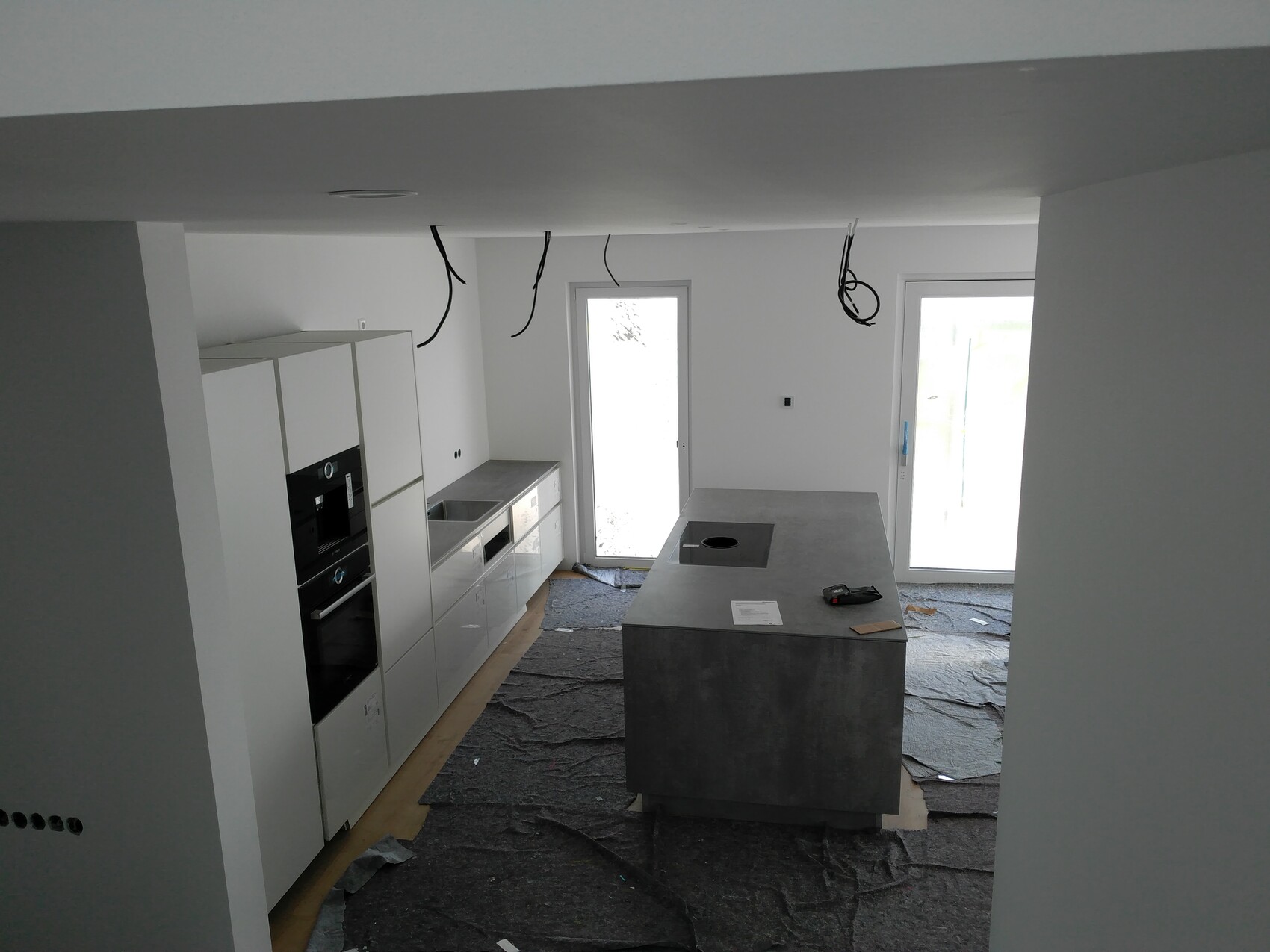 Moderne weiße Küche im Bau: Insel mit Kochfeld, hängende Kabel, Bodenfolie.