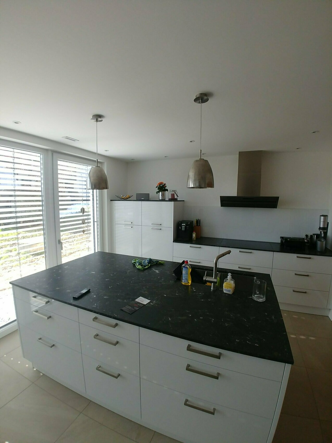 Moderne Küche mit einer Insel, weißen Schränken, Pendelleuchten und großen Fenstern.