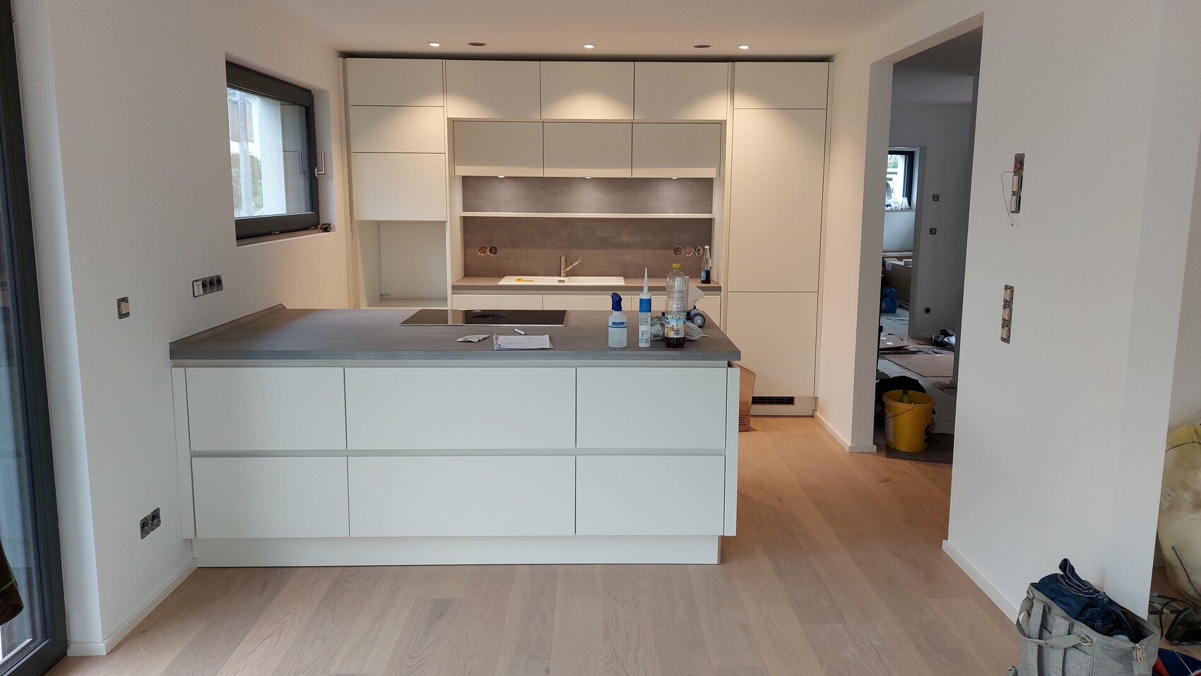 Moderne weiße Küche mit Insel, grauer Arbeitsplatte und unfertige Bauarbeiten.