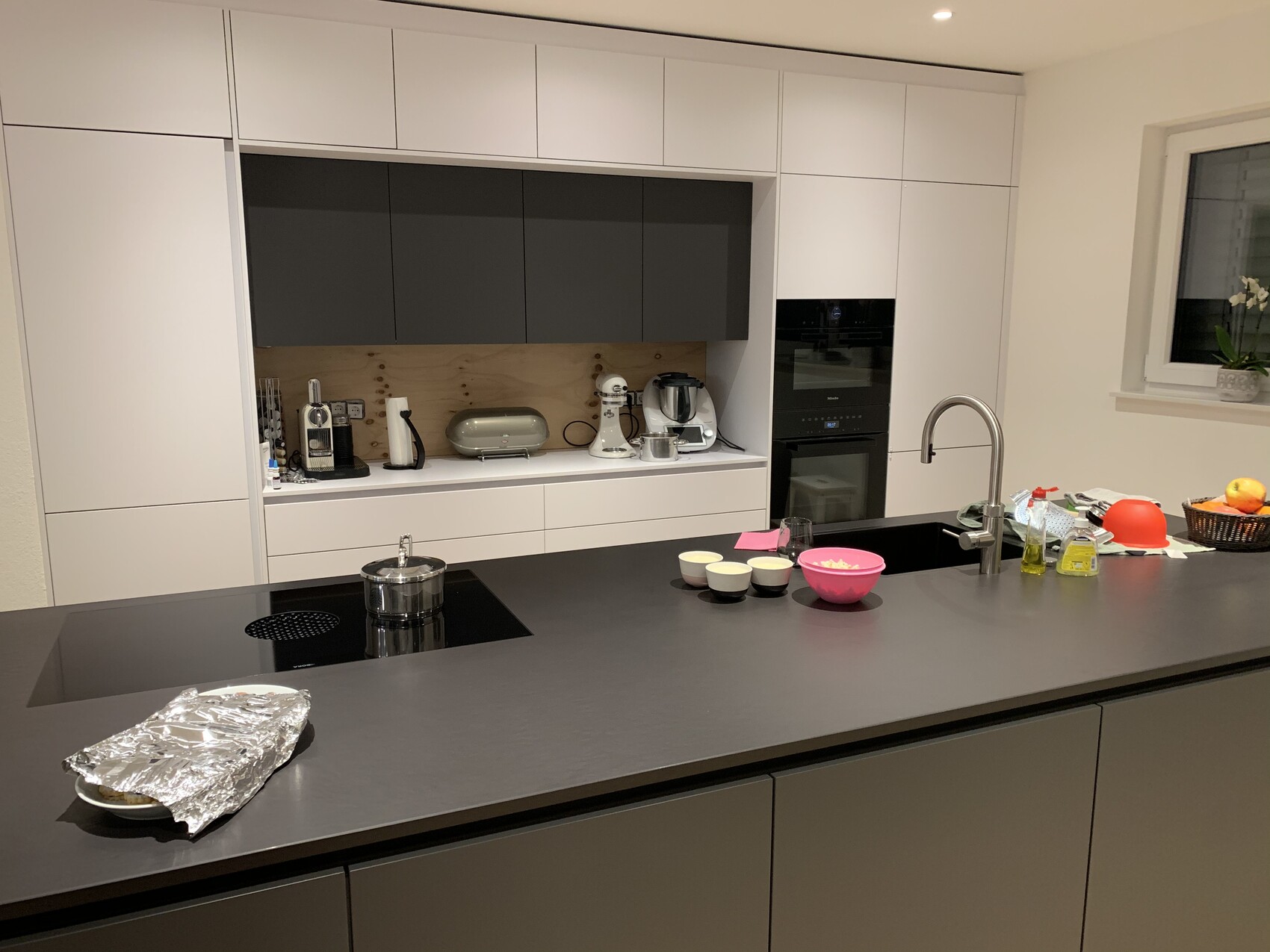 Moderne Küche mit zentraler Insel, Spüle, Cerankochfeld, Backofen und Küchenutensilien.