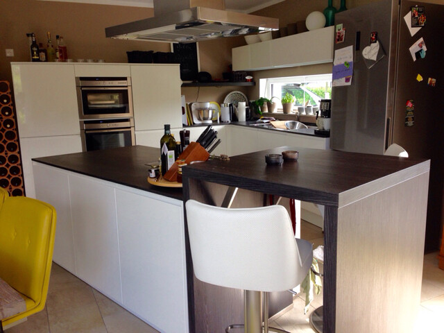 Moderne Küche mit Insel, weißen Schränken, Backofen und Kühlschrank.