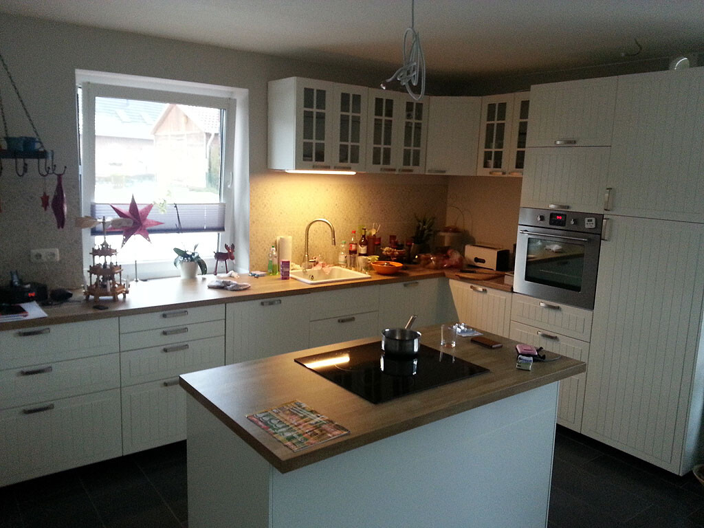 Moderne Küche mit Kücheninsel, Spüle, weißen Hängeschränken und Backofen.