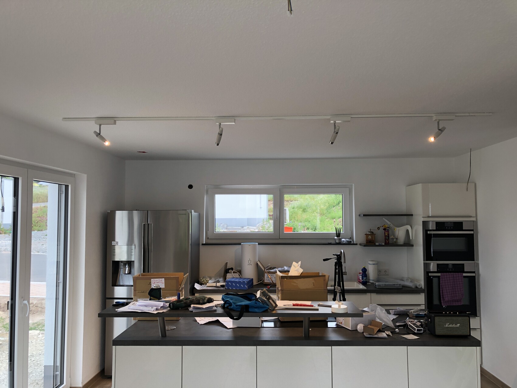 Moderne Küche mit Insel, Kühlschrank links, Backofen rechts, viele Utensilien auf Arbeitsfläche.
