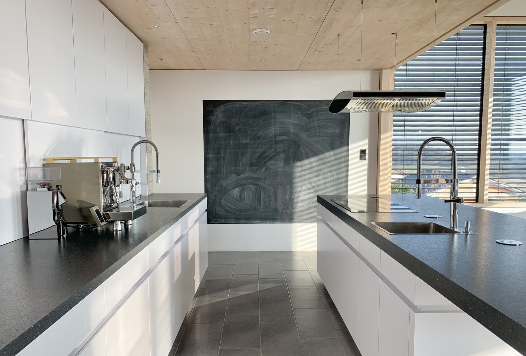 Moderne Küche mit weißen Schränken, schwarzen Arbeitsplatten, Kochinsel und Tafelwand.