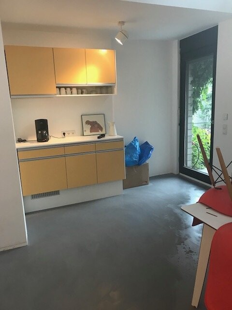 Küchenbereich mit gelben Schränken, Kaffeemaschine, Regal mit Tassen, Bild, blaue Taschen, Glastür.