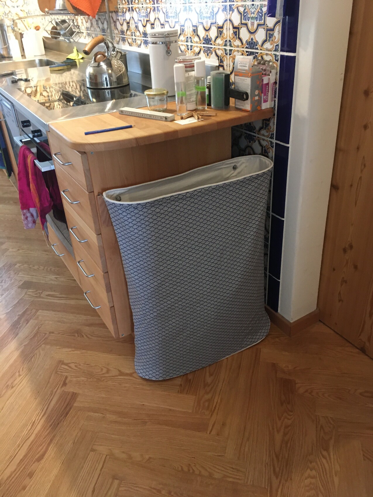Küche mit Holzinsel; daneben steht ein grauer Stoff-Wäschekorb mit Muster.