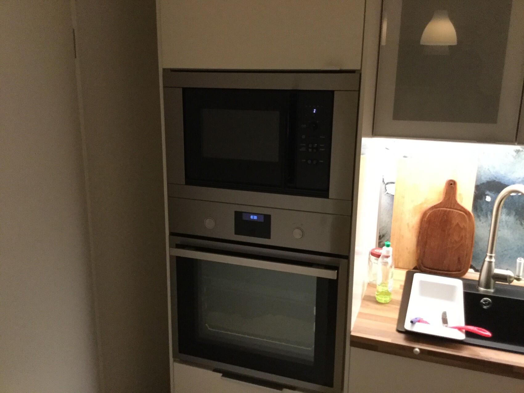 Küchenwand mit Mikrowelle über dem Ofen; rechts Spüle, Schneidebrett und Spülmittel.