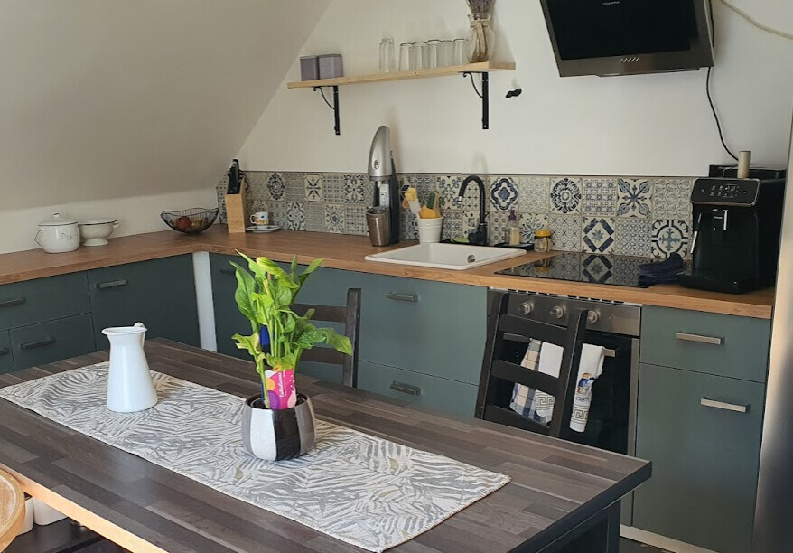 Küche mit grün-blauen Unterschränken, Holzplatte, Spüle, Ofen, Kaffeemaschine; Tisch mit Pflanze