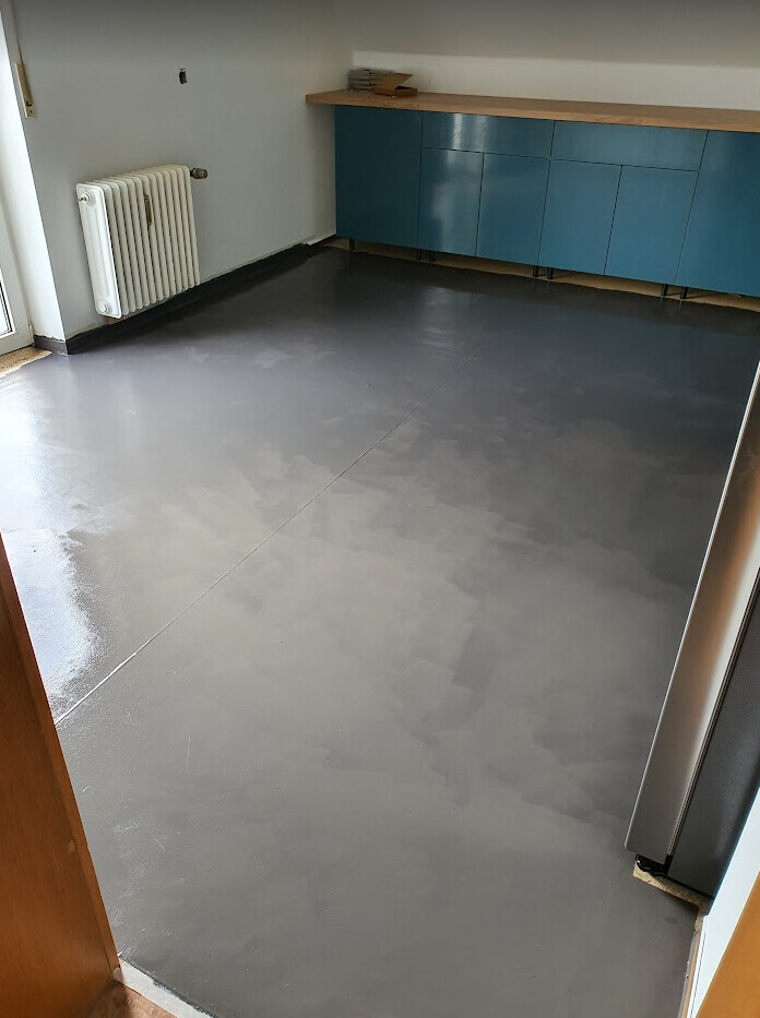 Raum mit blauen Unterschränken und Holzarbeitsplatte, grauer Epoxidboden, Heizkörper links.