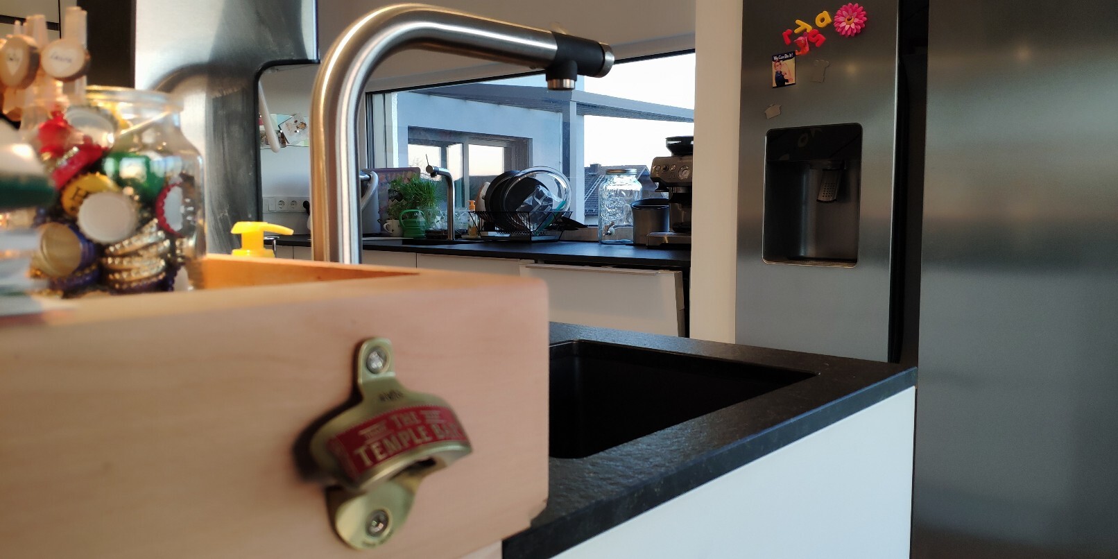 Moderne Küche mit Spüle, Armatur, Geschirr und Kühlschrank im Hintergrund.