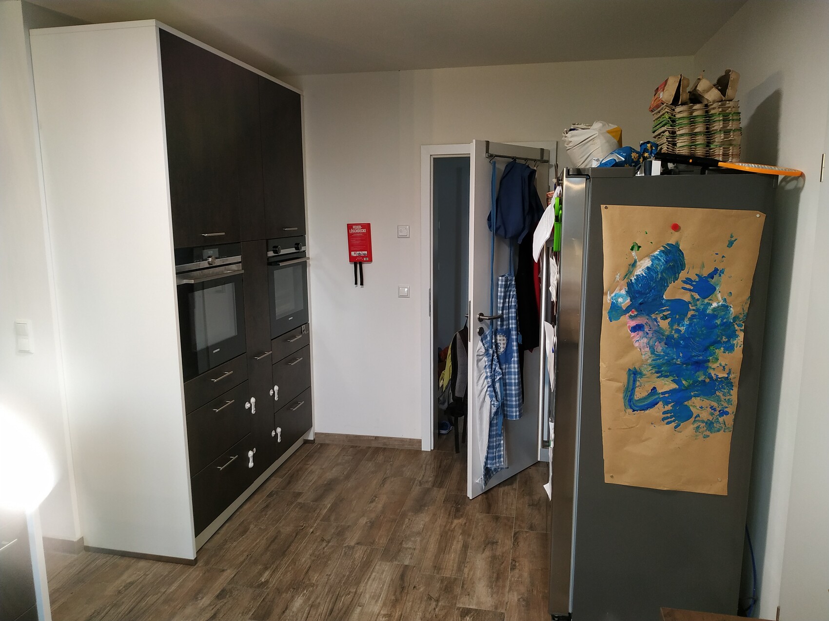 Moderne Küche mit dunklen Einbaugeräten links, Kühlschrank rechts, bemaltes Papier auf der Tür.