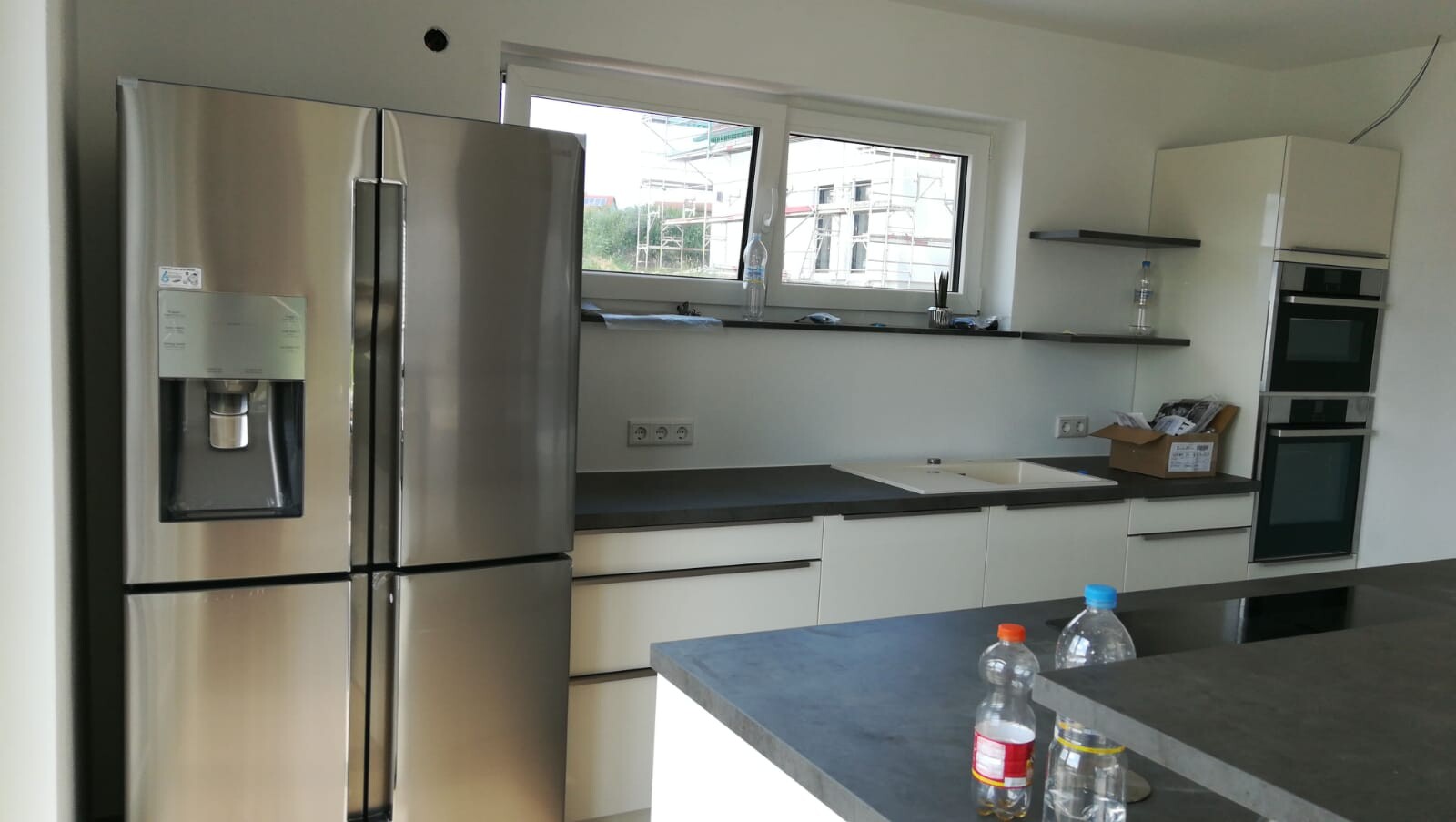Moderne Küche mit Edelstahl-Kühlschrank, Spüle, Insel und Einbau-Backöfen.