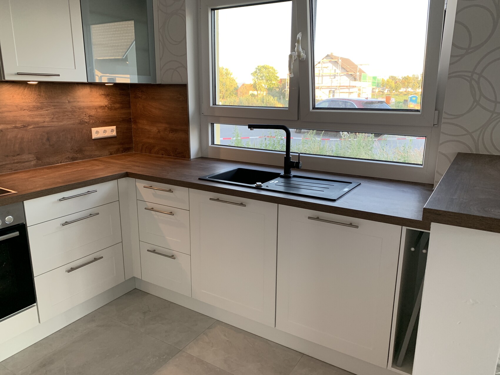 Moderne L-förmige Küchenzeile mit weißen Schränken, brauner Holzplatte, Spüle unterm Fenster.
