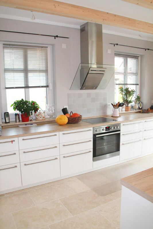 Moderne Küche mit weißen Schränken, Backofen, Dunstabzug, Obstkorb und Pflanzen.