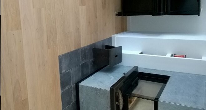 Moderne Küche mit Einbauherd, grauen Arbeitsplatten und dunklen Fliesen.
