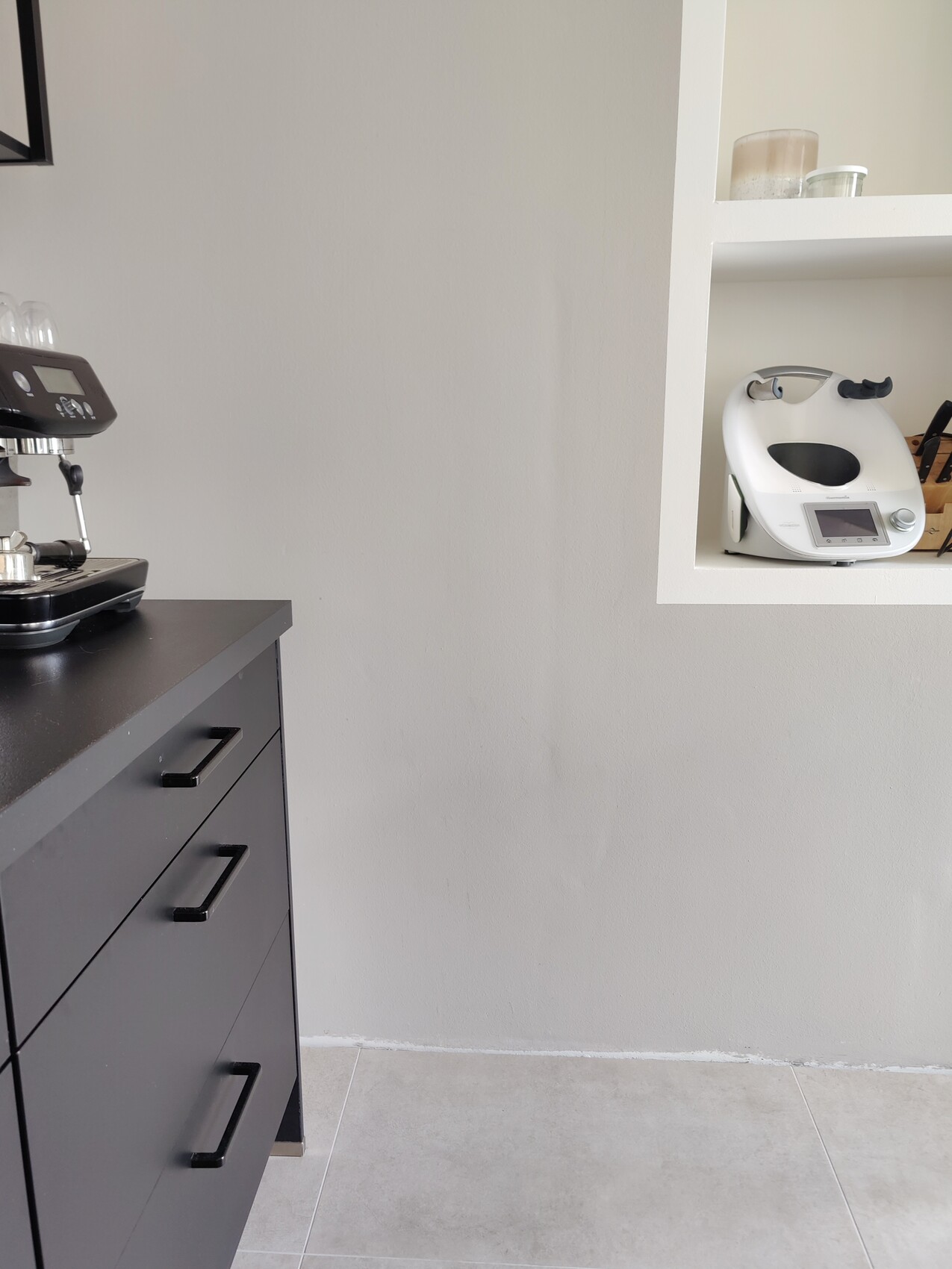 Küche: schwarze Kommode mit Espressomaschine links; weiße Küchenmaschine im Wandregal rechts.