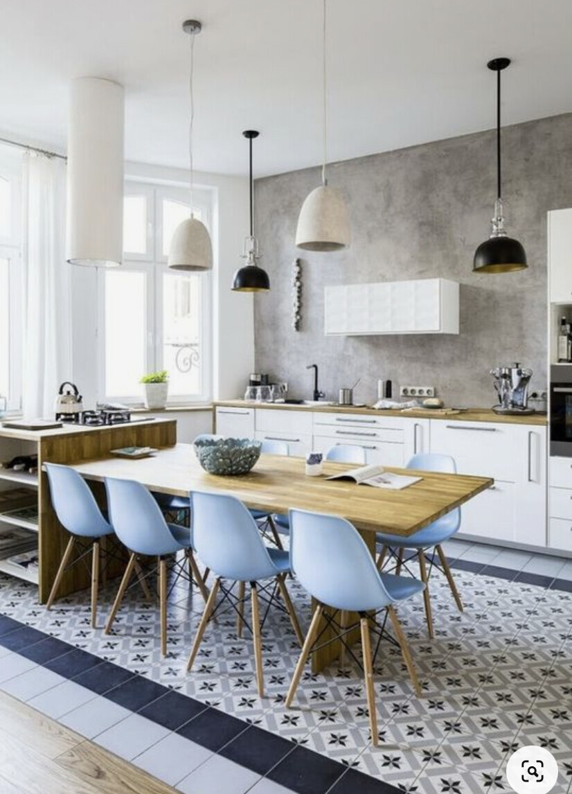 Moderne Küche mit langem Holztisch, hellblaue Stühle, grauer Wand und geometrischen Bodenfliesen.