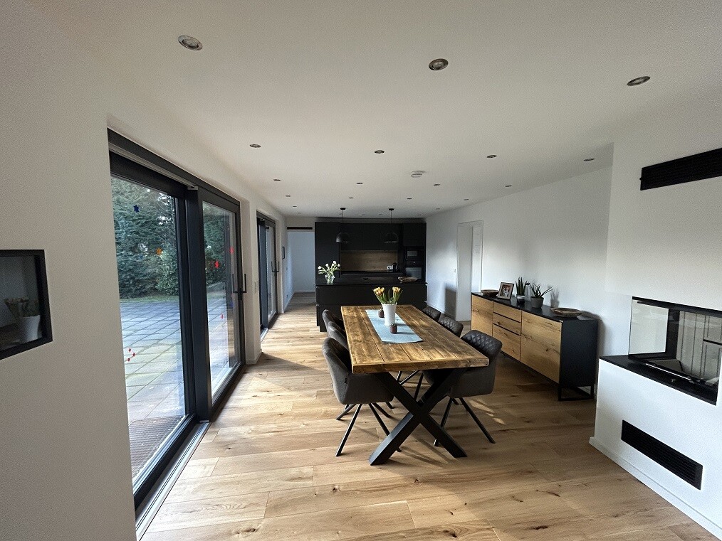 Offener Essbereich mit Holztisch, grauen Sesseln, Glas-Schiebetüren und moderner Küche.