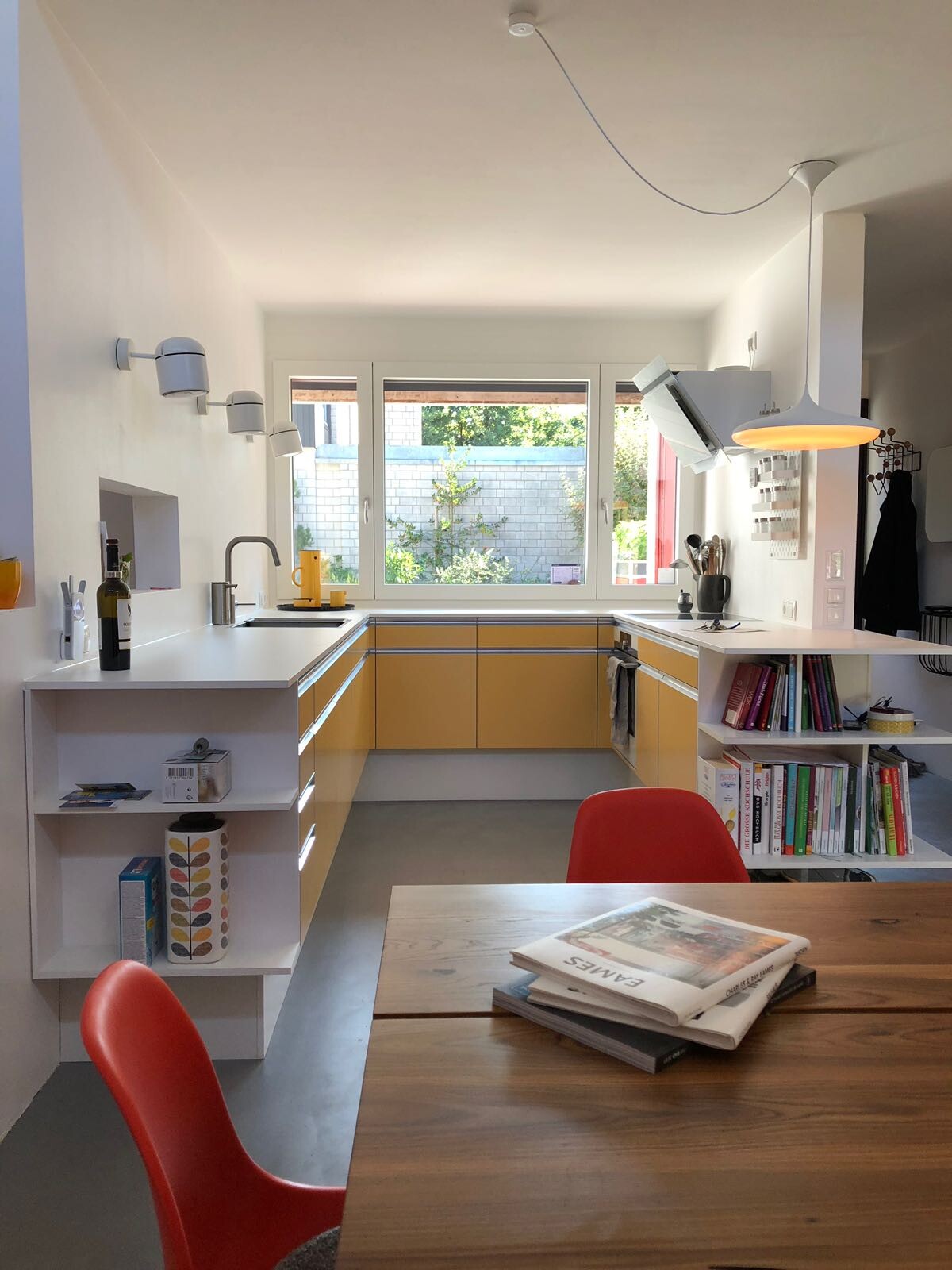 Moderne Küche mit weißen Wänden, gelben Unterschränken, Holztisch und roten Stühlen.