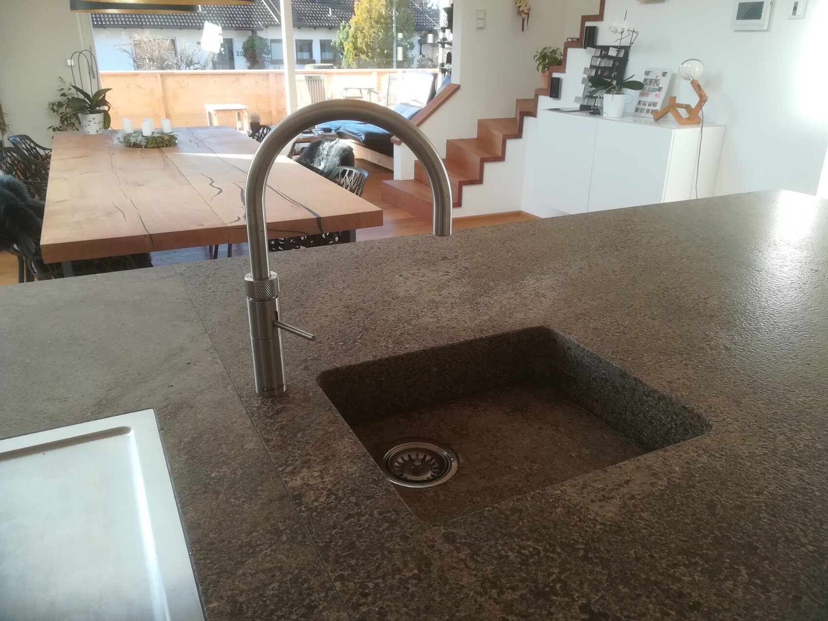 Moderne Küche mit Granitarbeitsfläche, Spüle, hohem Wasserhahn; Treppe und Esstisch im Hintergrund.