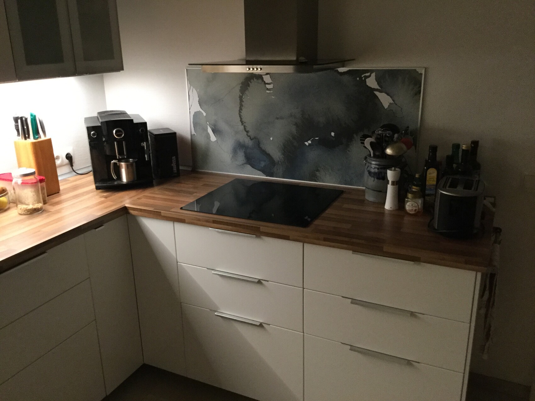 Moderne Küche mit Holzplatte, Induktionskochfeld, weißen Schränken und blaugrauer Rückwand.