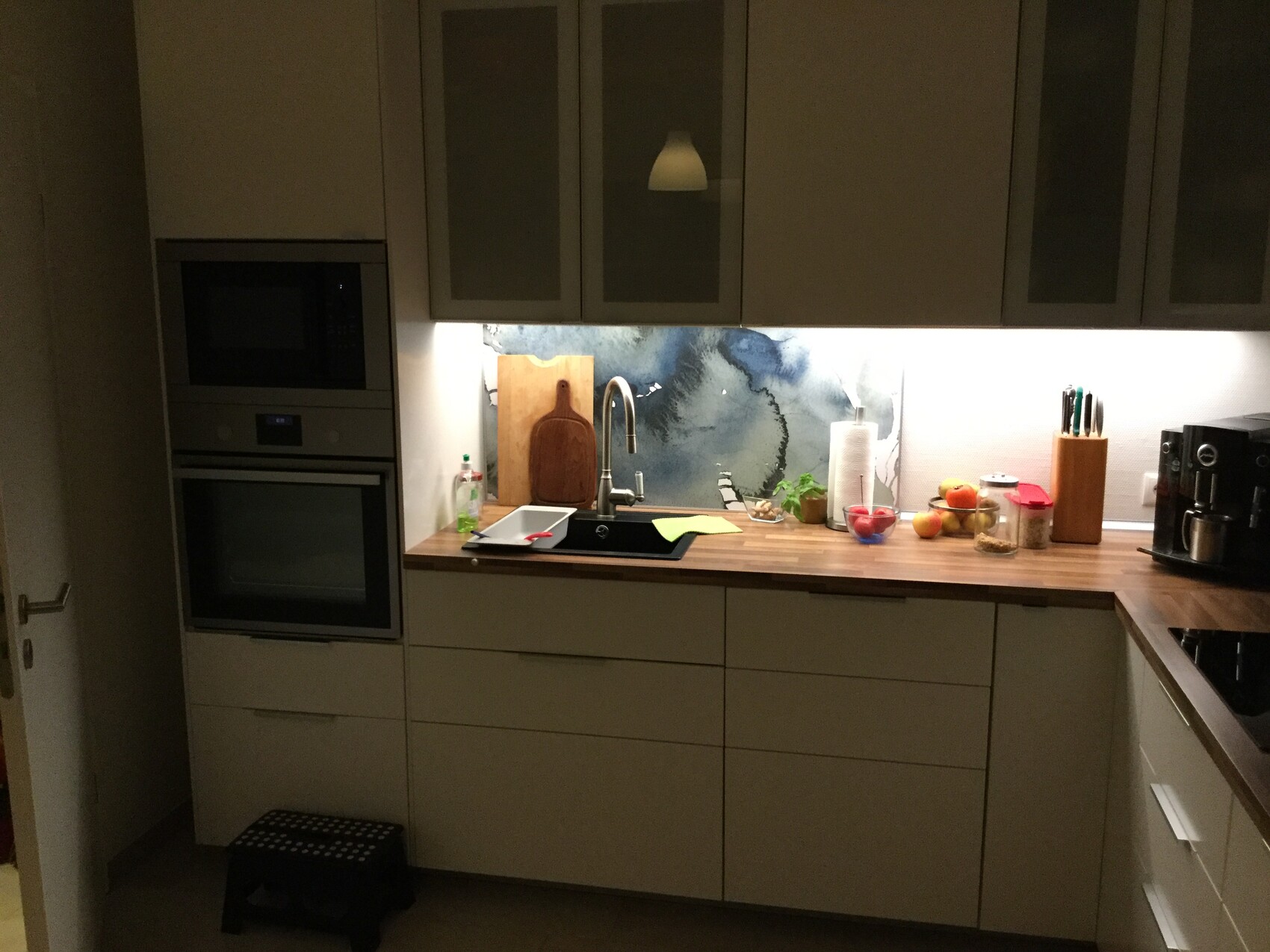 Moderne Küche mit Spüle, Holzarbeitsplatte, Obstkorb, Messerblock, Backofen und Kaffeemaschine.