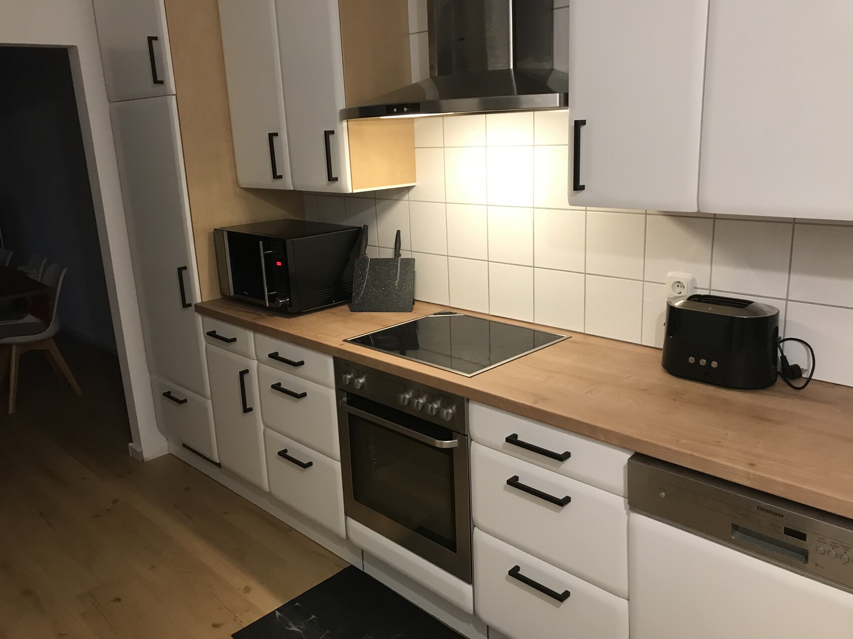 Moderne Küche: weiße Schränke, Holzarbeitsplatte, Induktion, Backofen, Mikrowelle, Toaster.