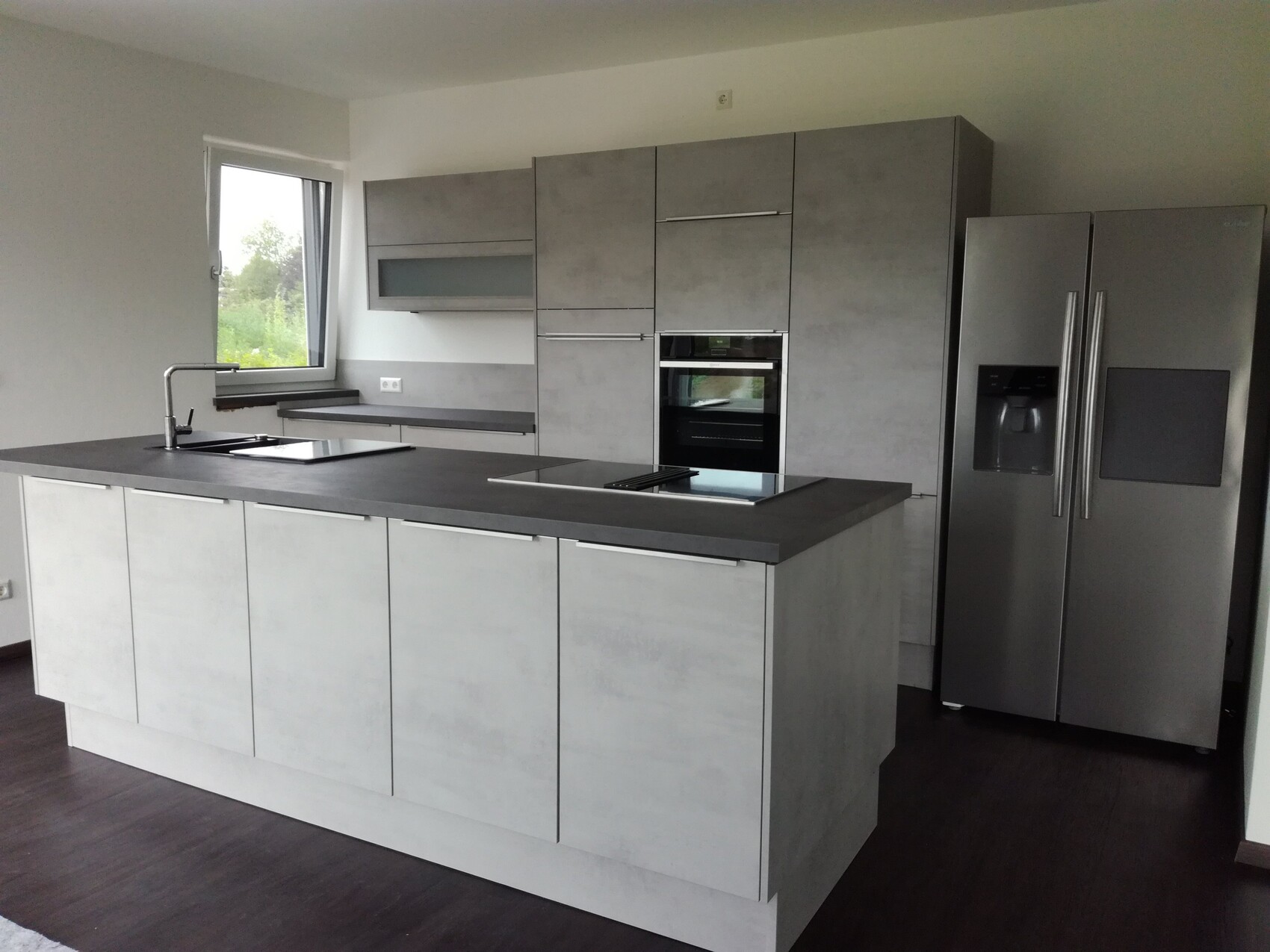 Moderne Küche mit grauer Kücheninsel, Einbauofen, Side-by-Side Kühlschrank und Fenster