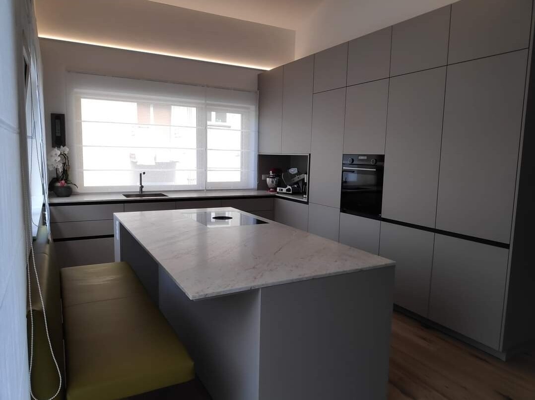 Moderne graue Küche mit zentraler Marmorkochinsel, Spüle am Fenster und integrierten Geräten.