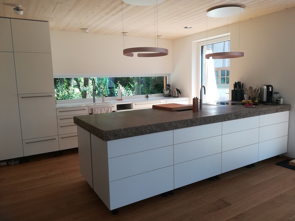 Moderne Küche mit großer Insel, Steinplatte, weißen Schränken und Holzboden.