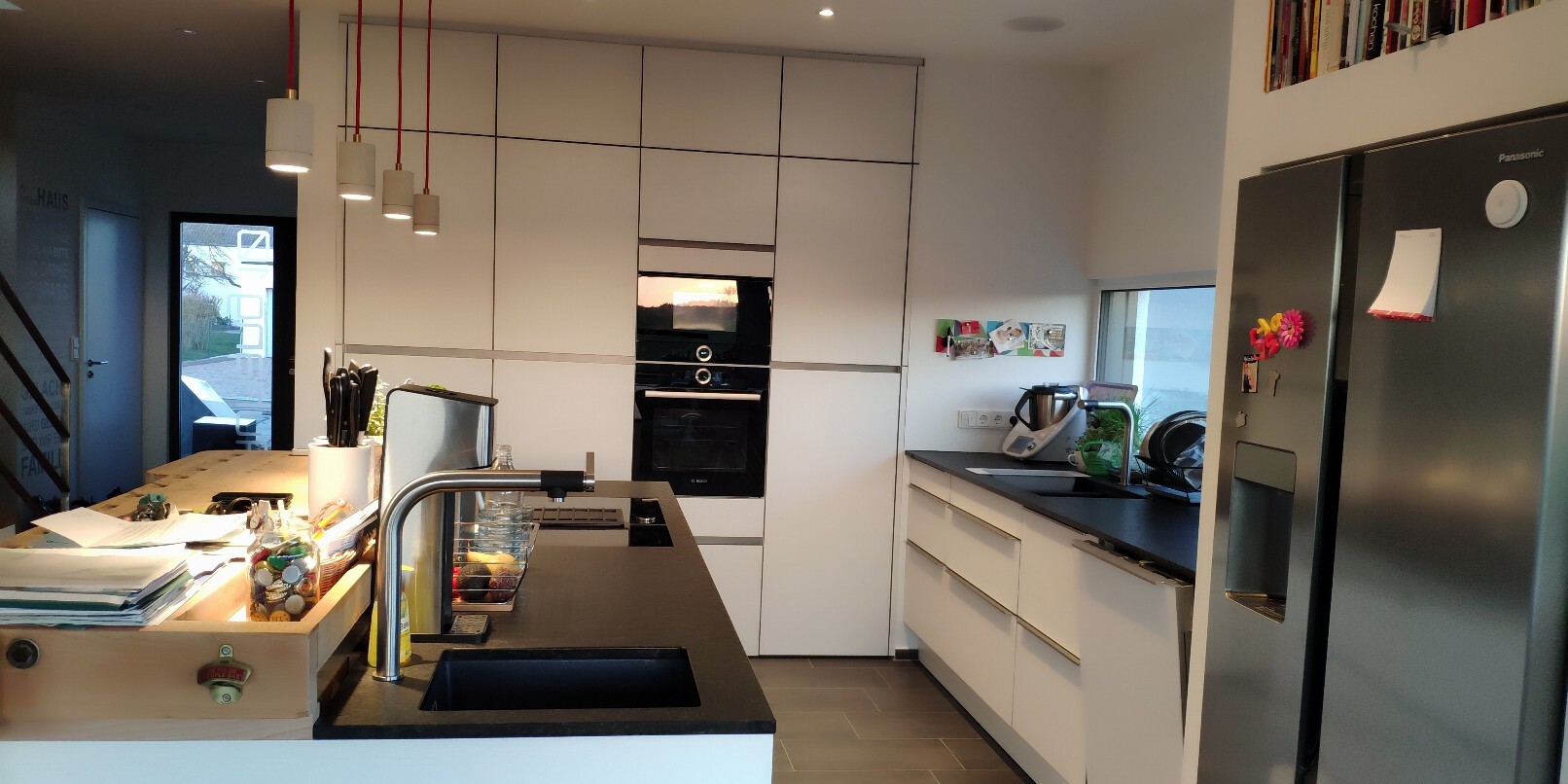 Moderne weiße Küche mit Insel, integriertem Backofen, Kühlschrank und Spüle.