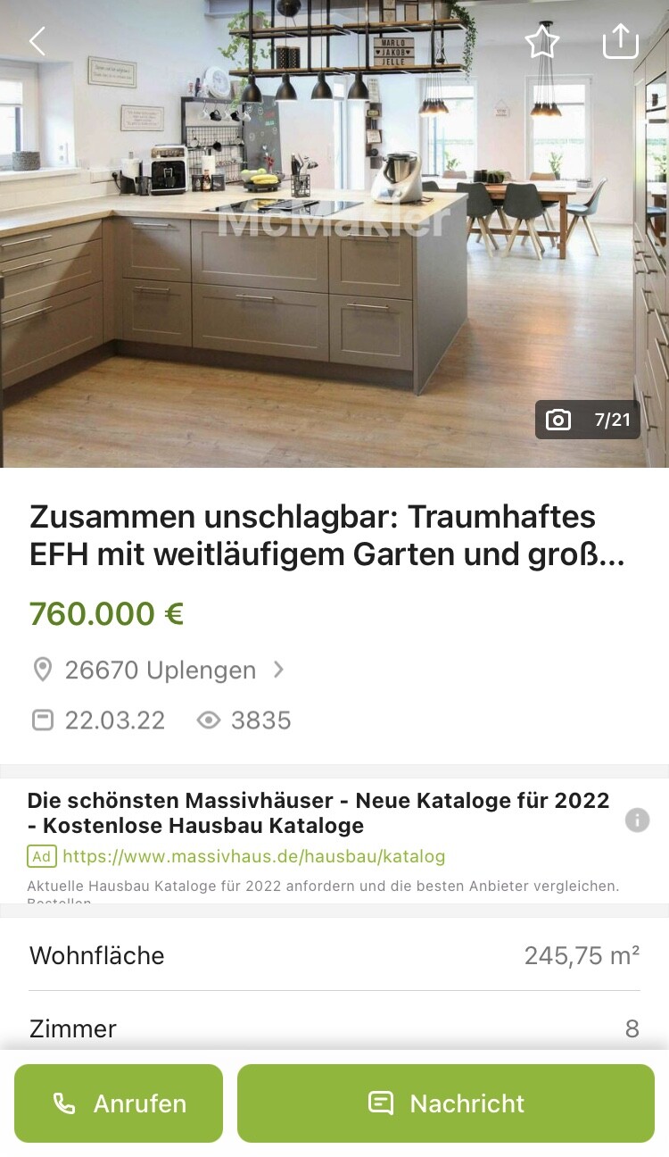 Moderne offene Küche mit Kochinsel, grauen Unterschränken, Holzfußboden und Esstisch im Hintergrund.