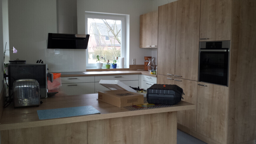 Moderne Küche mit Holzschränken, Insel und Backofen; Kartons stehen auf der Theke.