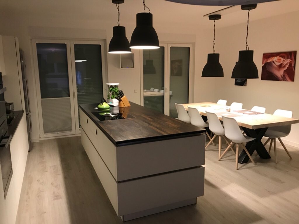 Moderne Kücheninsel mit dunkler Holzplatte und Esstisch mit weißen Stühlen