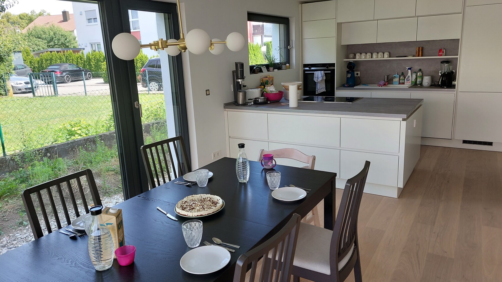 Moderne Küche mit Esstisch und Insel; Tisch mit Kuchen, Gläsern und Wasserflasche.