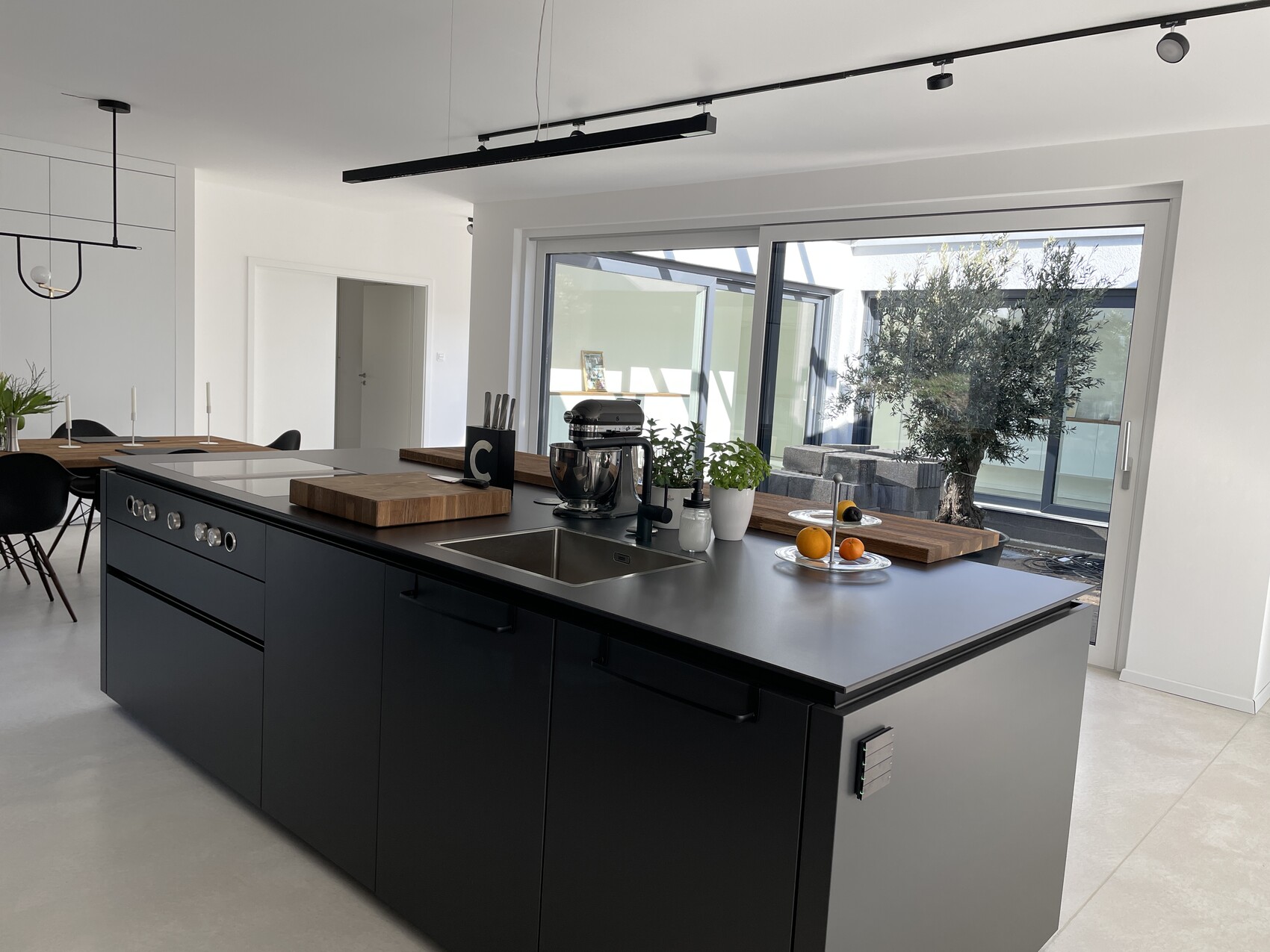 Moderne Kücheninsel in Schwarz mit Spüle, Holzbrett, Mixer, Obstschale und Zugang zum Garten.