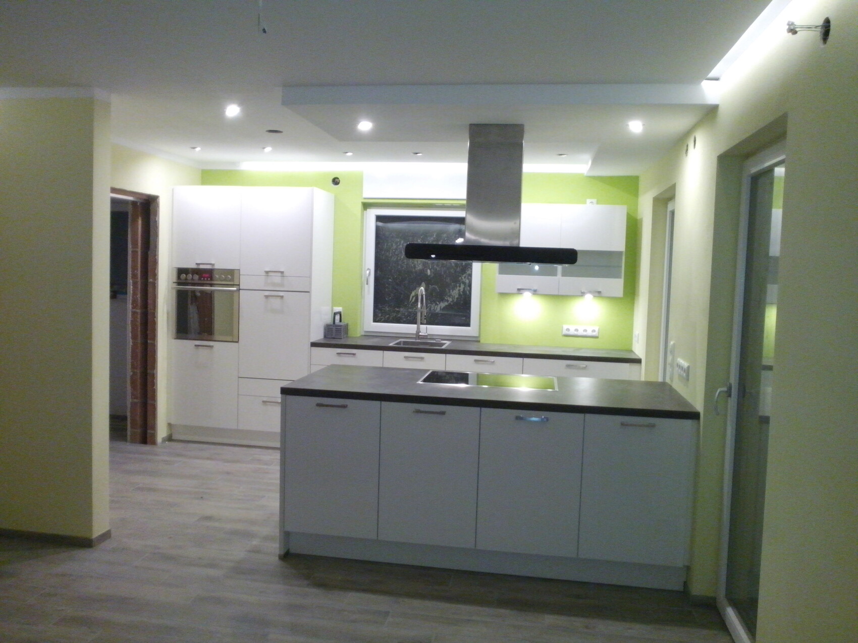 Moderne Küche mit weißen Schränken, Kücheninsel, Ofen und grüner Wand.