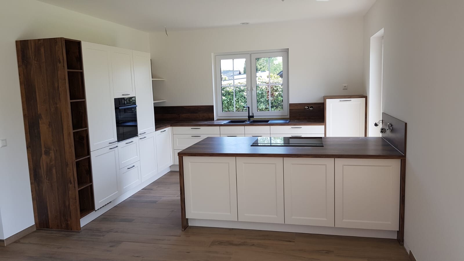 Moderne Küche mit weißen Schränken, Holzarbeitsplatten, Kochinsel und Fenster über Spüle.