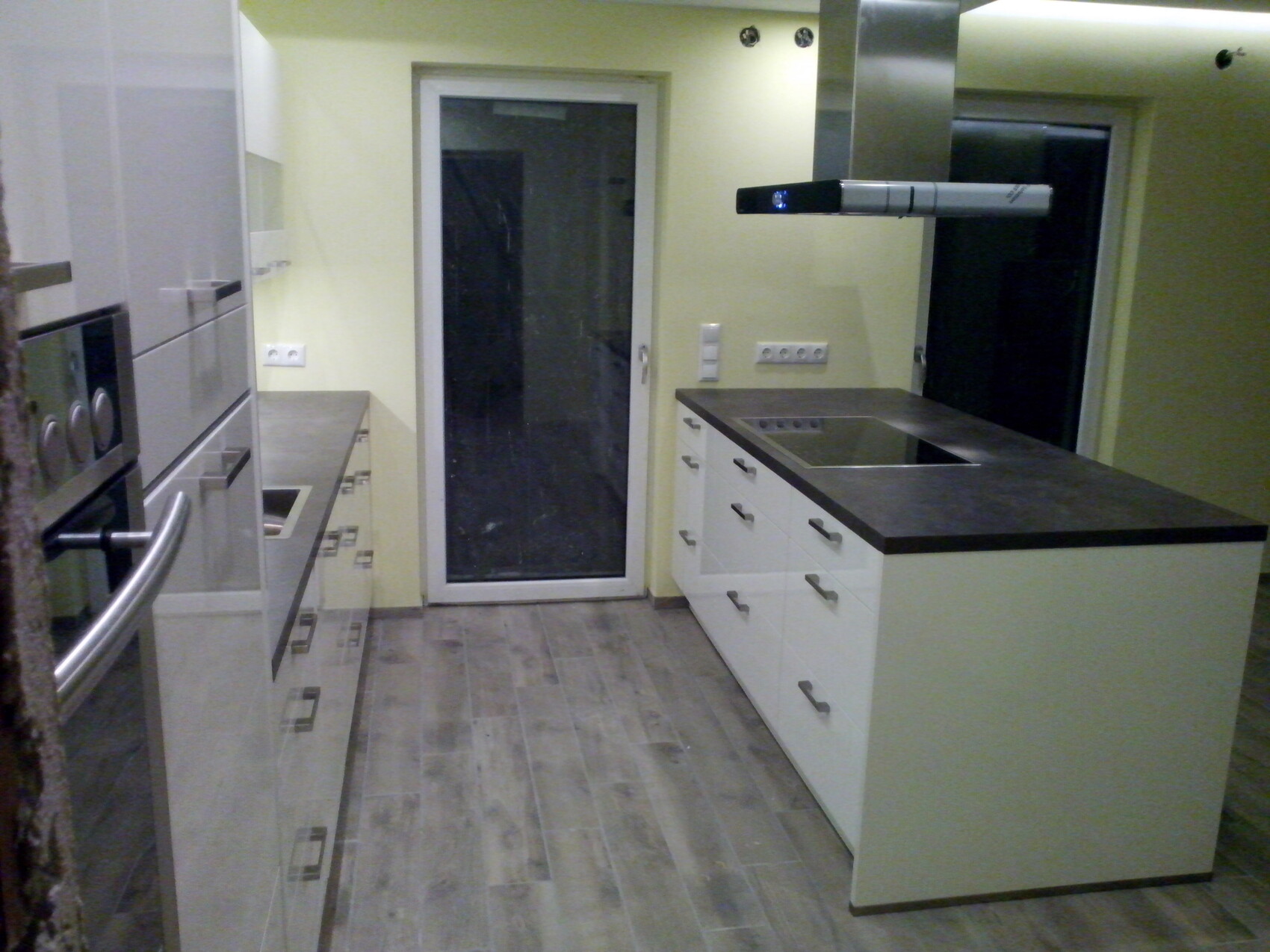 Moderne Küche mit Insel, weißen Schränken, schwarzen Arbeitsplatten und Glastür.