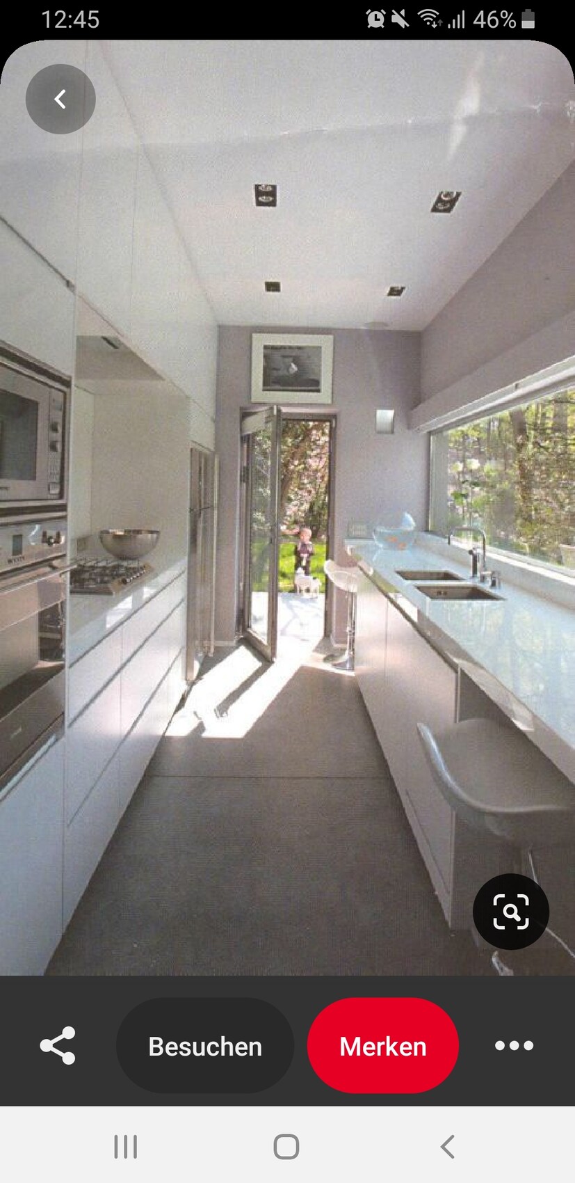 Moderne weiße Küche mit Insel, Spüle und Barhockern; offene Tür zum Garten, viel Licht.