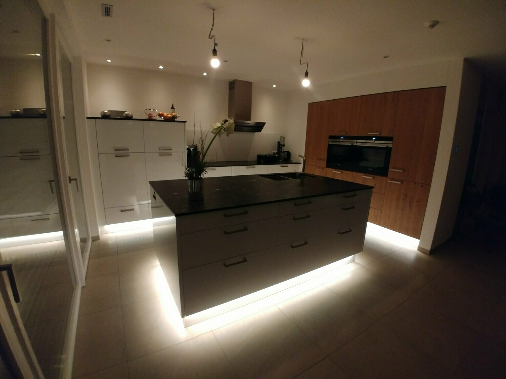 Moderne Küche mit dunkler Insel, weißen Unterschränken, Holzfronten und Backofen.