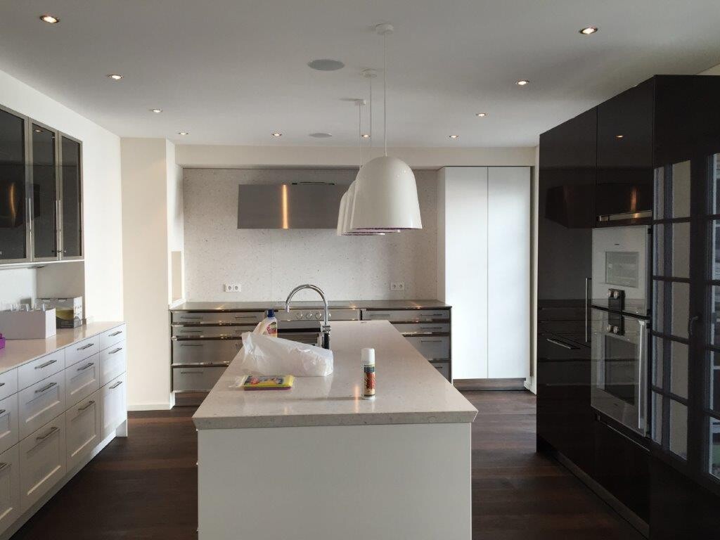 Moderne Küche mit weißer Insel, Spüle, Armatur, Edelstahlgeräten und dunklen Schränken.