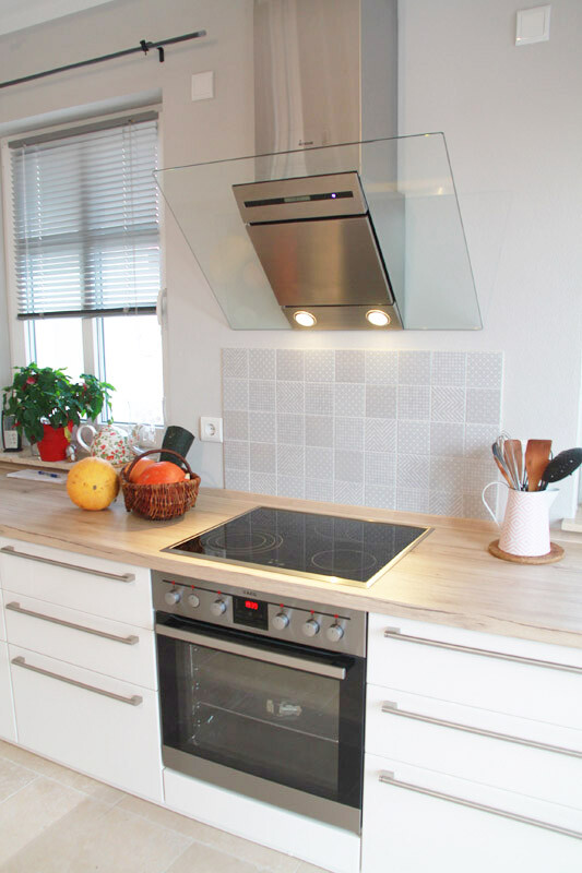 Moderne Küche mit Glas-Dunstabzug, Induktionskochfeld, Backofen, Obstkorb und Pflanze.